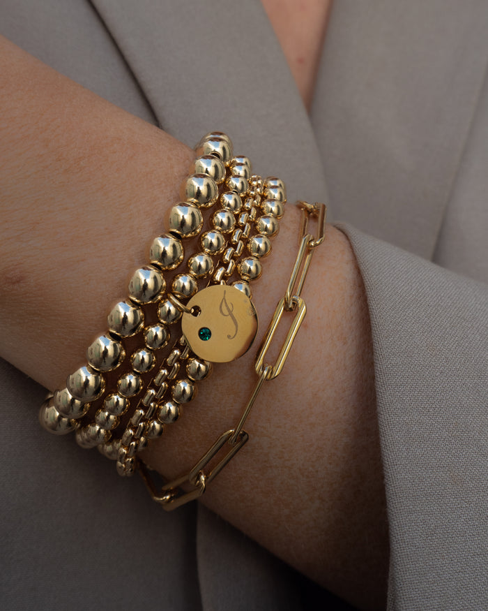 Close up of a wrist in a grey blazer with assorted gold bracelets