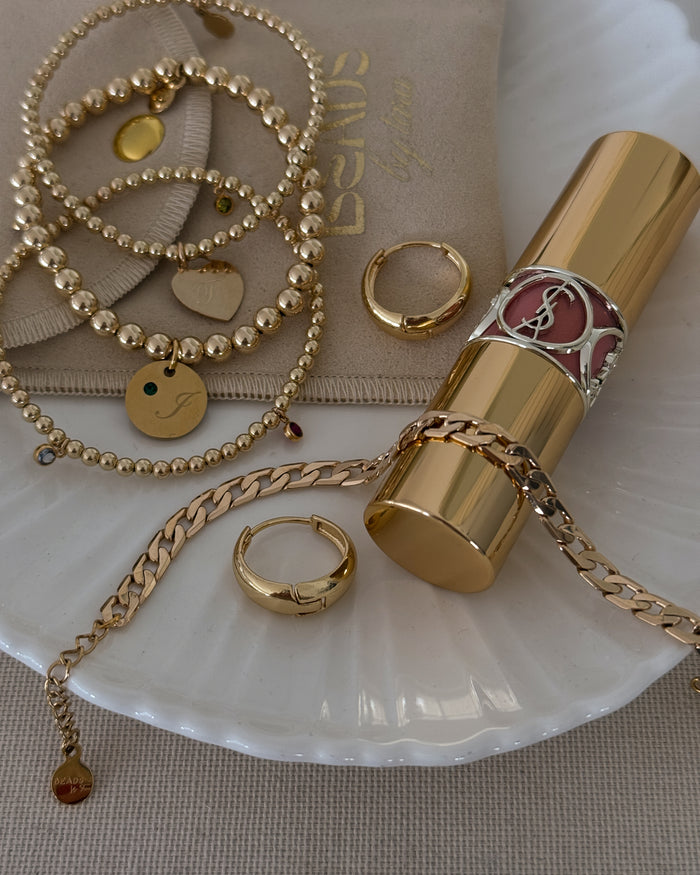 Assorted gold jewelry and lipstick on a white tray