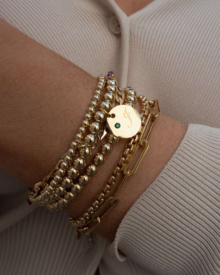 Close up of a wrist in a white sweater with assorted gold bracelets