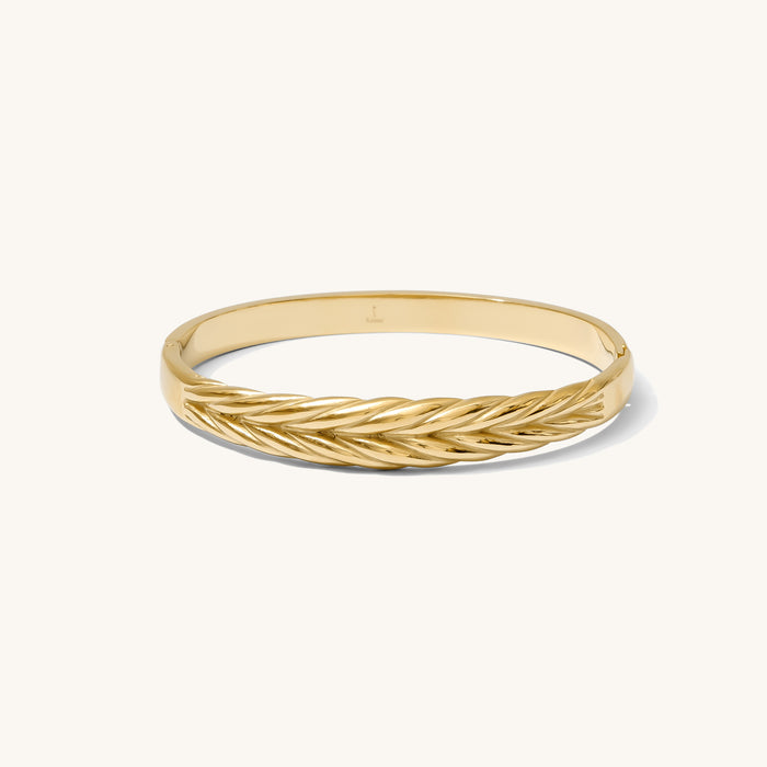 Close up of woven gold bangle on a white background