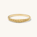 Close up of woven gold bangle on a white background