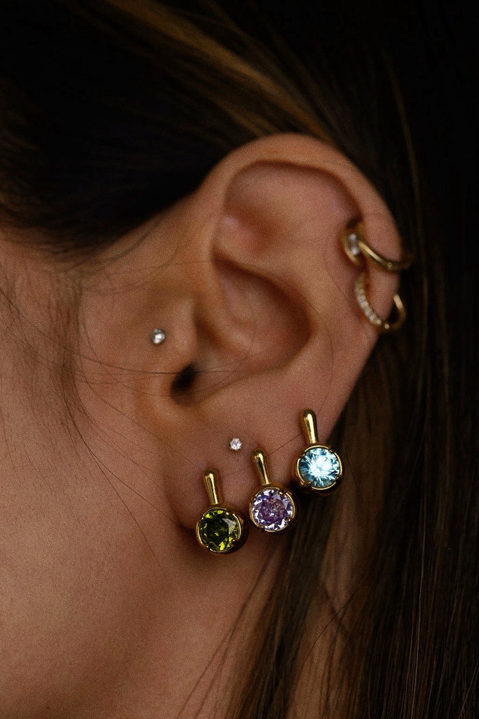 Close-up of an ear with multiple gold and multicolored diamond earrings.