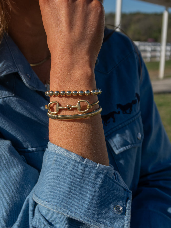 Close-up of a person's wrist wearing multiple bracelets with a blue denim jacket in the background.