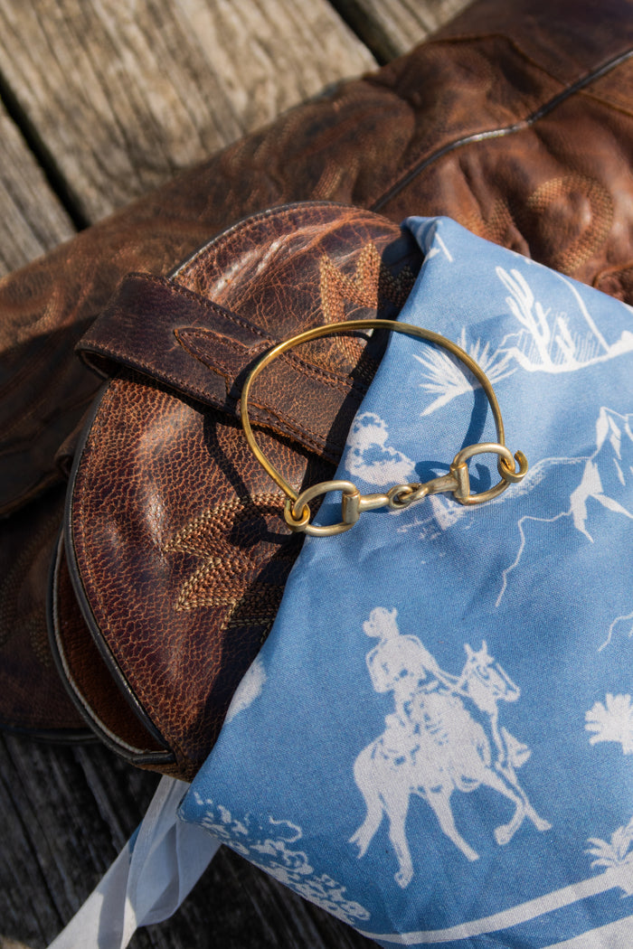 Brown leather bag with a gold ring on top of a blue fabric with white patterns.