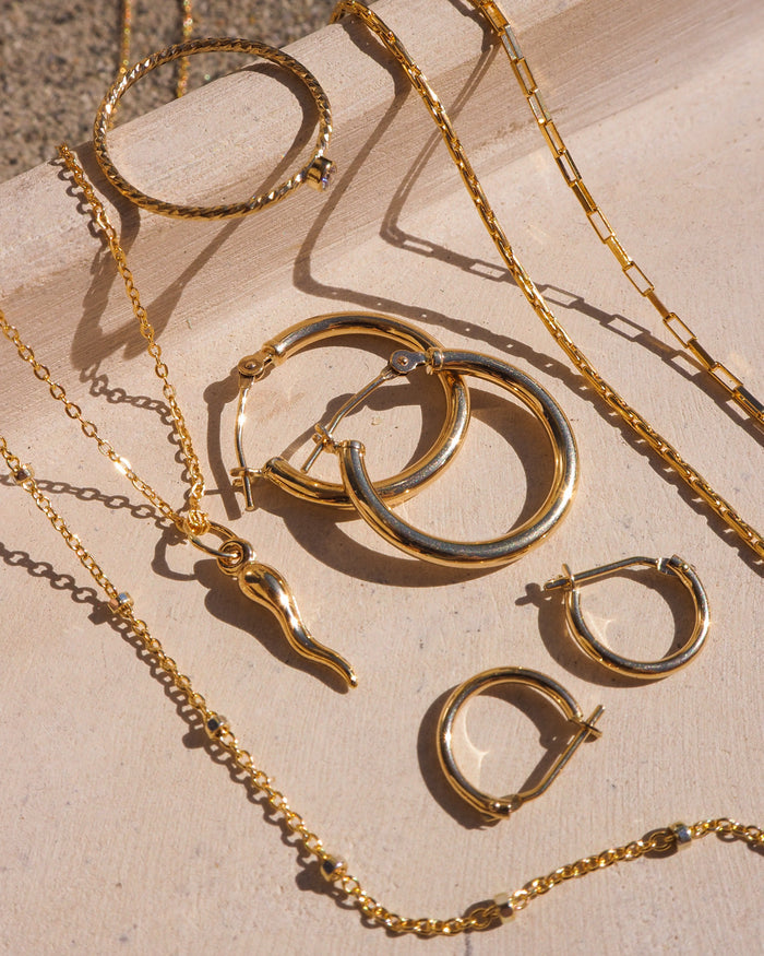 Multiple gold necklaces and earrings laid on a neutral surface
