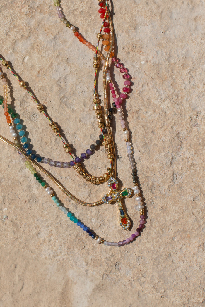 Gold bead accents flanking the jewel-toned cross of the Caliente necklace