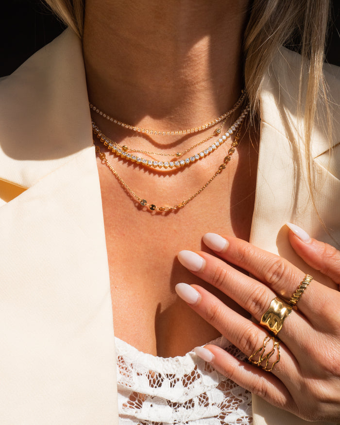 Model wearing the gold Carissa tennis necklace layered with dainty chains