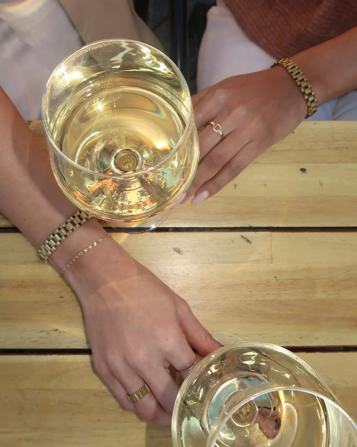 Two glasses of wine on a table held by two wrists with gold jewelry