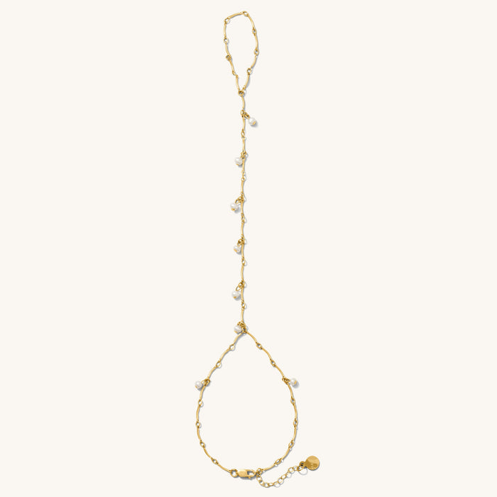 Close up of gold hand chain with pearl accents on a white background