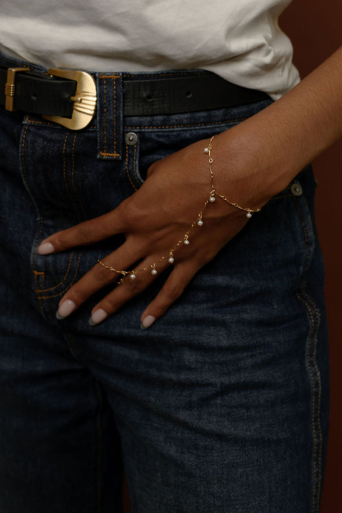 Close up of person wearing a white shirt, blue jeans, and gold hand chain