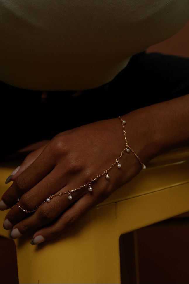 Close up of a hand wearing a gold hand chain resting on a yellow chair