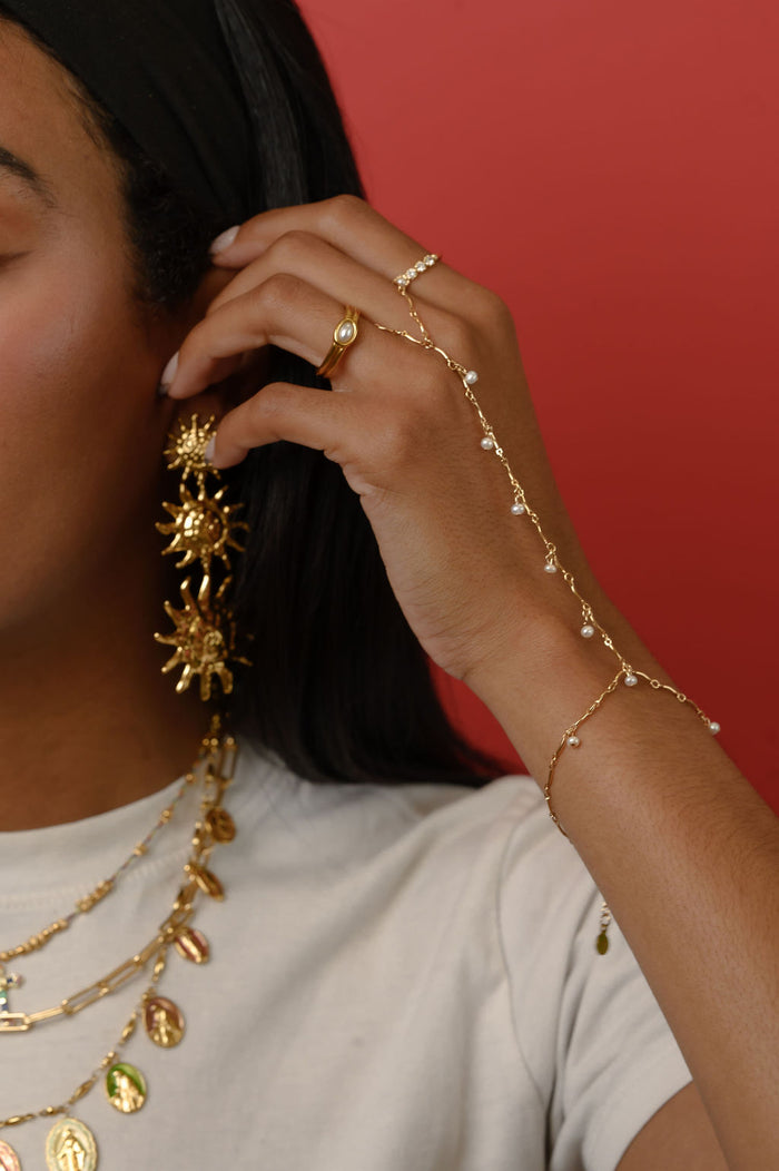 Close up of a person wearing statement gold rings, necklaces, and a hand chain on a red background
