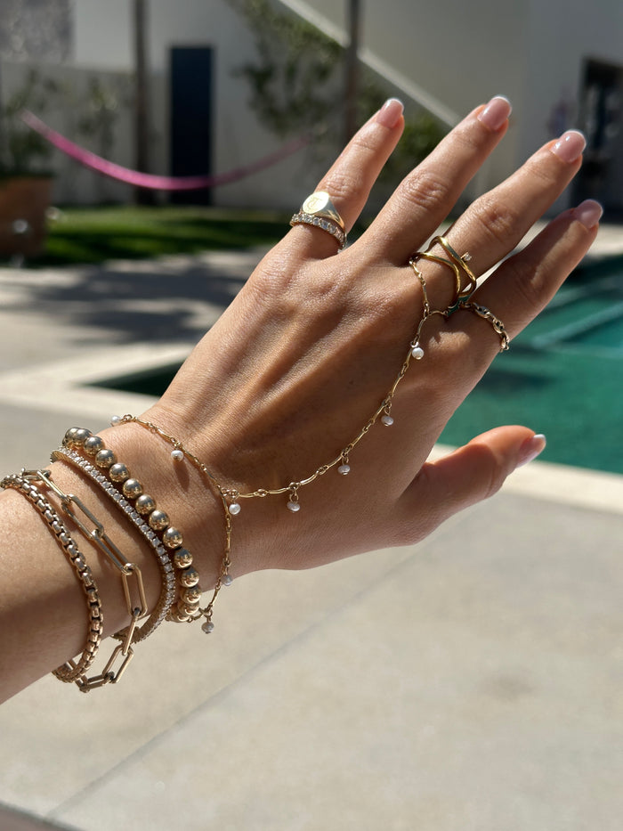 Close up of a hand with various gold rings and bracelets against a backyard