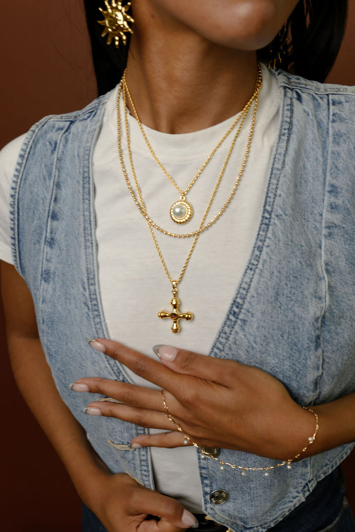 Close up of person wearing a white shirt, blue vest, and gold jewelry