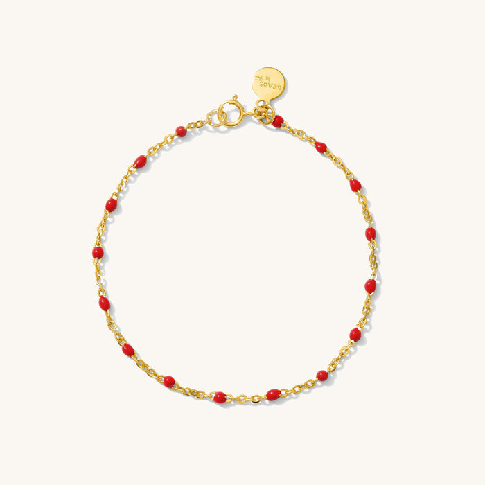 Close up of gold bracelet with red bead accents on a white background