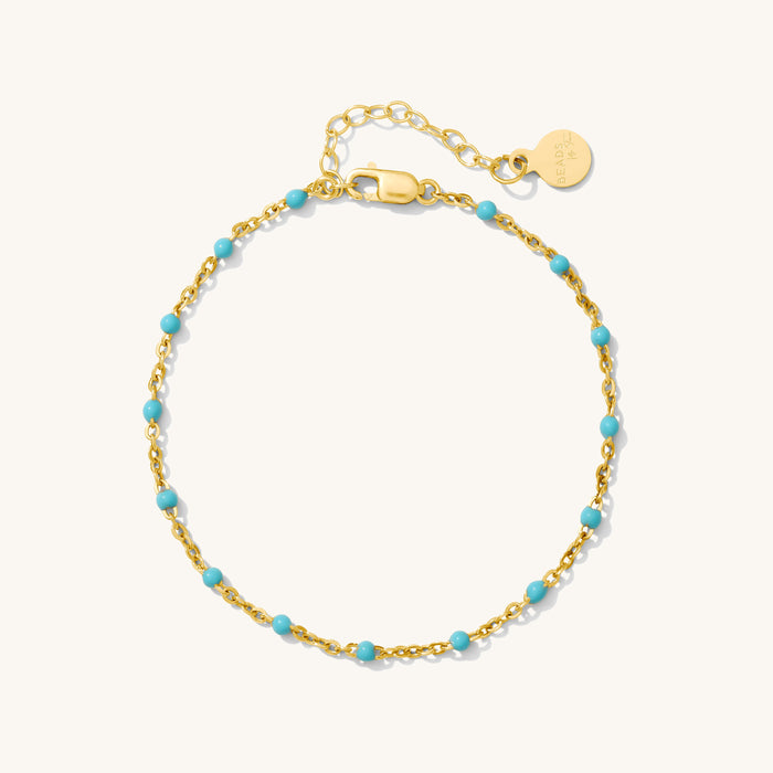 Close up of gold bracelet with teal bead accents on a white background