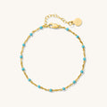 Close up of gold bracelet with teal bead accents on a white background