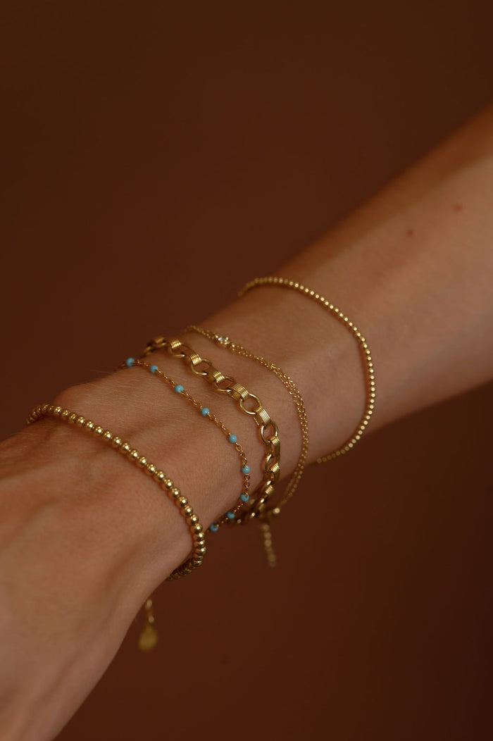 Close up of a wrist with assorted gold bracelets with stone accents on a brown background