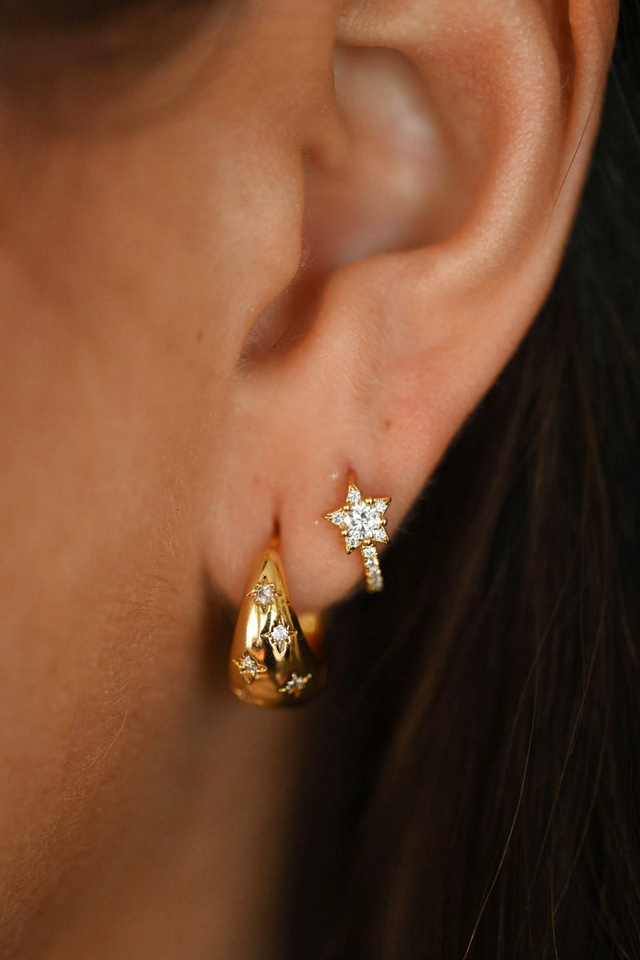 Close-up of an ear wearing gold earrings with a blurred background