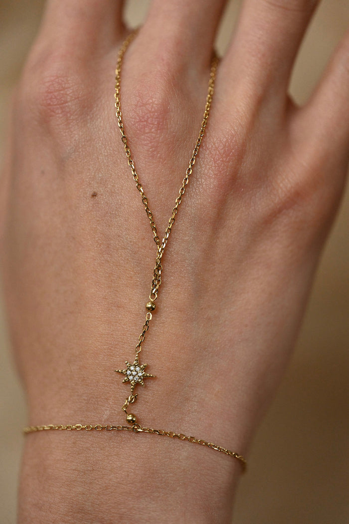 Gold bracelet with star design on a wrist against a neutral background