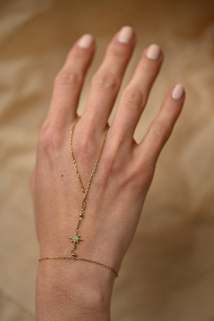 Hand wearing a delicate gold necklace with a star pendant on a beige background