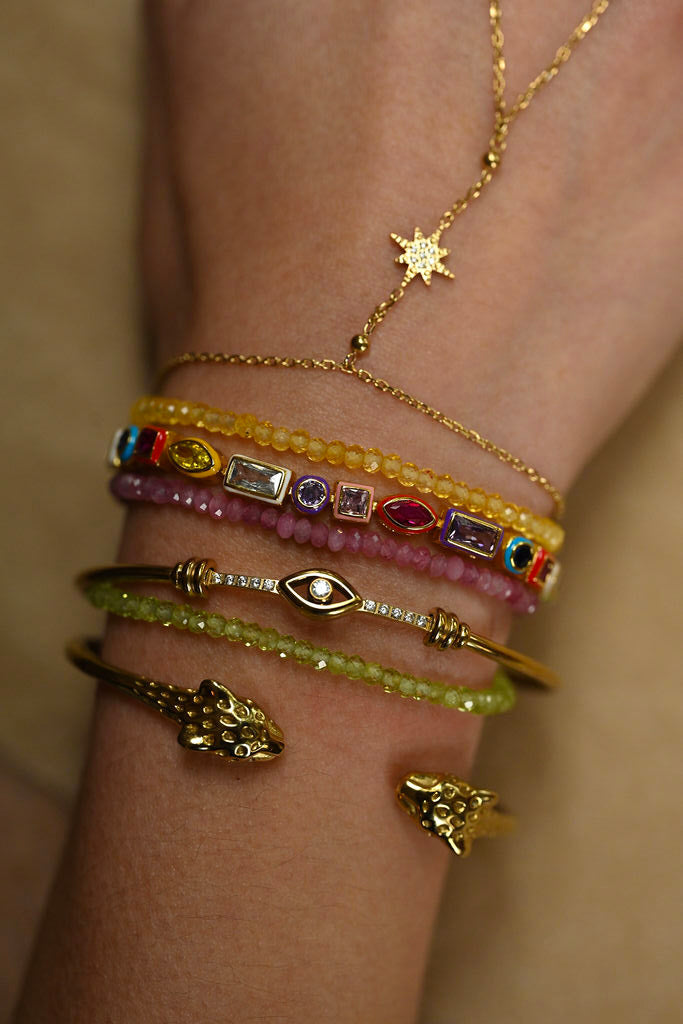 Close-up of a wrist wearing multiple gold and gemstone bracelets on a neutral background