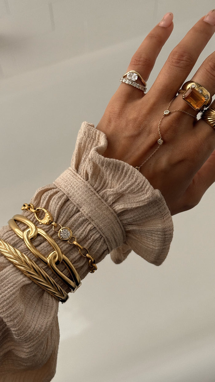 A wrist in a tan blouse wearing gold rings and bracelets