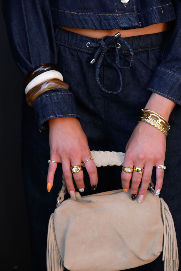 A person in a denim set wearing gold and stone bracelets and rings holding a purse