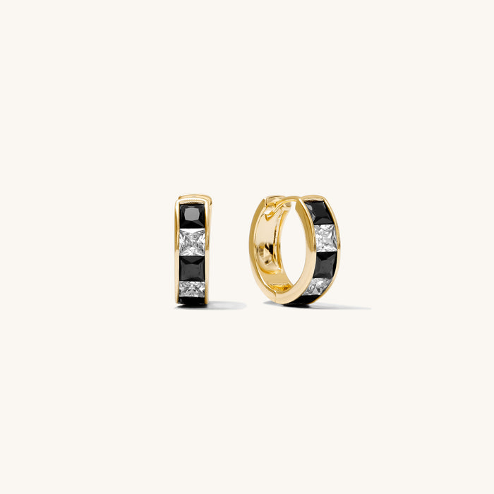 Close up of gold and black huggie earrings on a white background