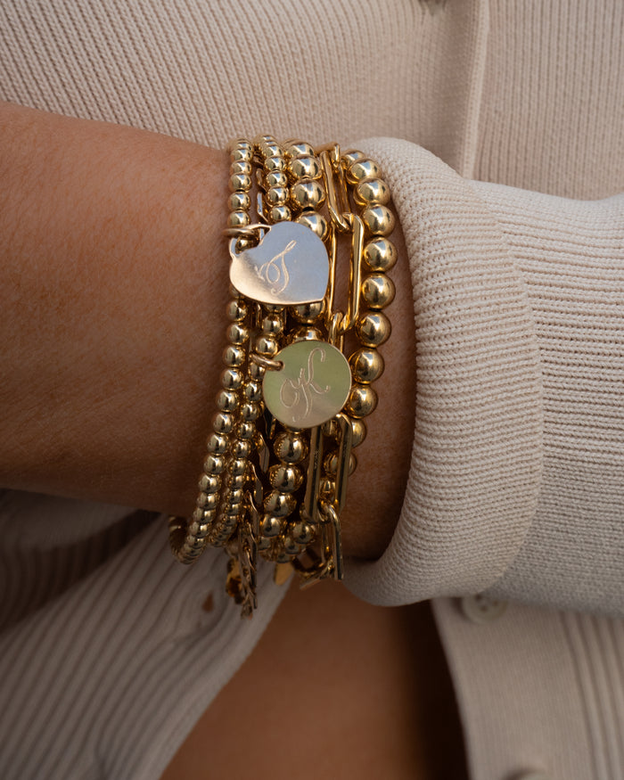 Close up of a wrist in a white sweater with assorted gold bracelets