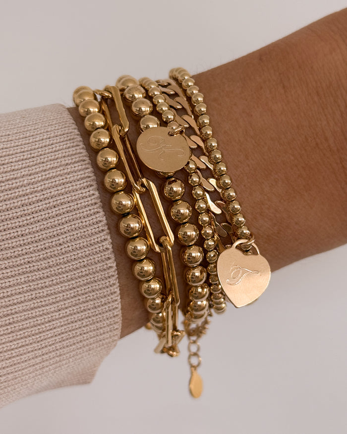 Close up of a wrist in a white sweater with assorted gold bracelets