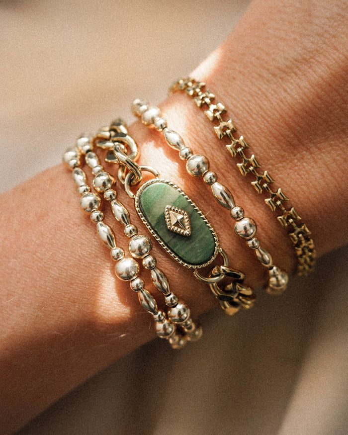 A wrist with assorted gold bracelets on a tan background