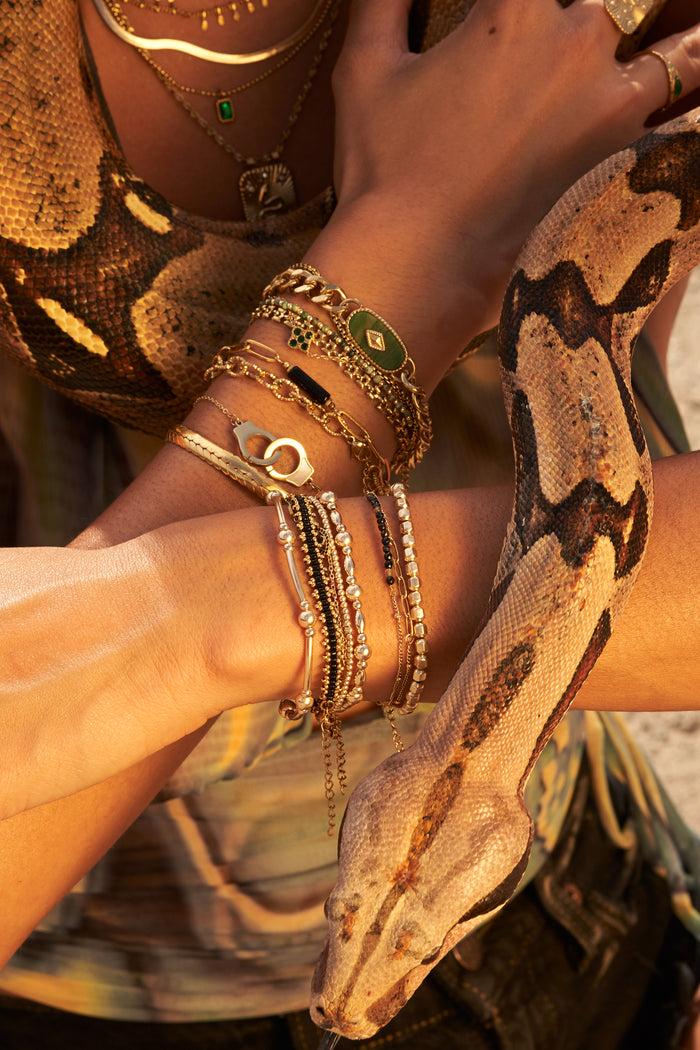 A person with a tan snake wrapped around them, wearing assorted gold necklaces, bracelets, and rings.