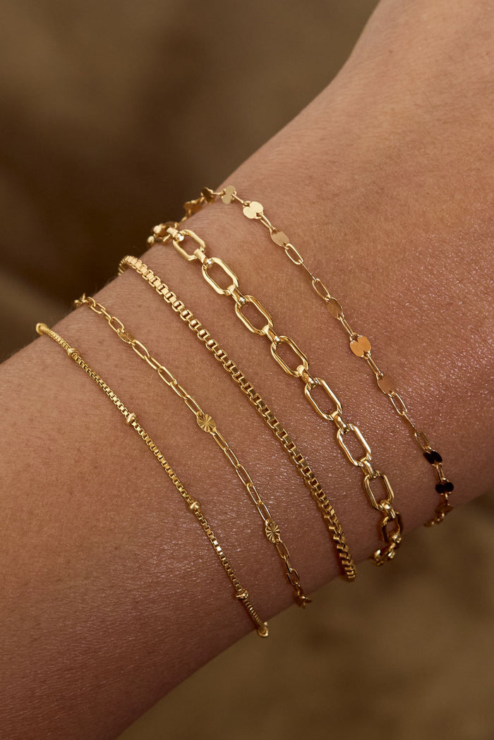 Close up of a wrist with dainty gold bracelets on a brown background