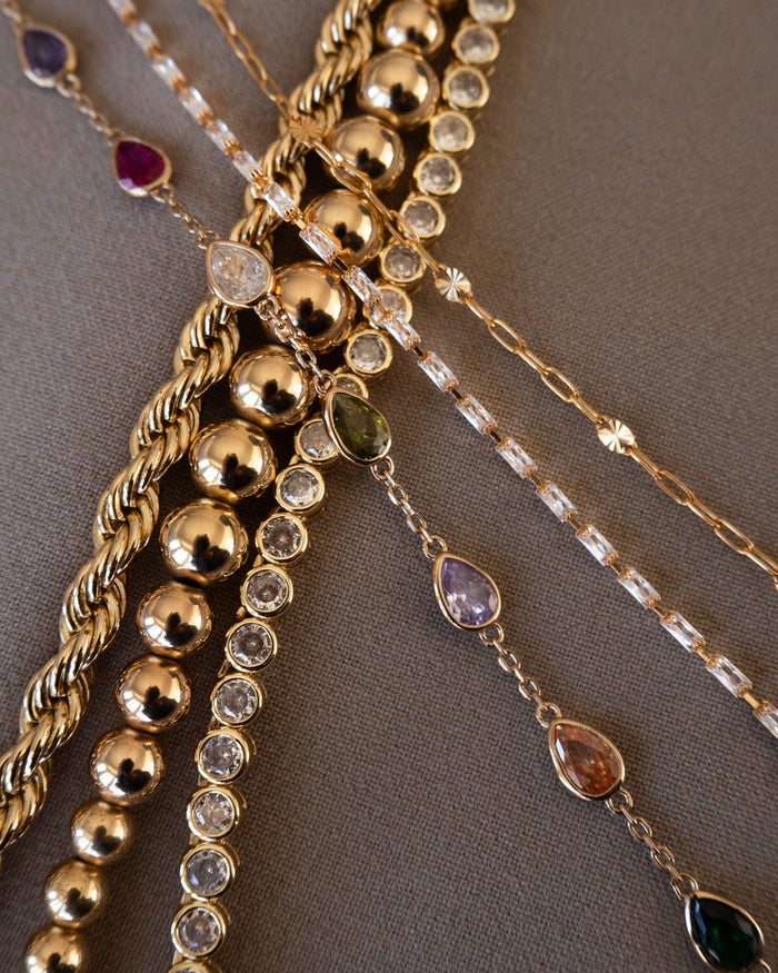 Close up of various gold and stone bracelets on a taupe background