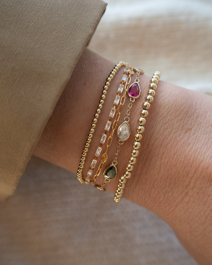 Close up of a wrist in a blazer with assorted gold and stone bracelets on a neutral background
