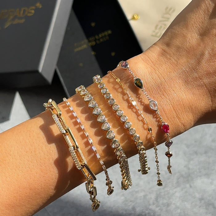 Close up of a wrist with gold and stone bracelets on a grey background