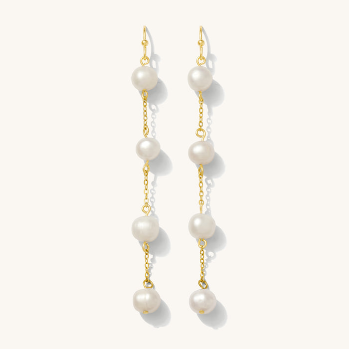 Close up of gold pearl drop earrings on a white background
