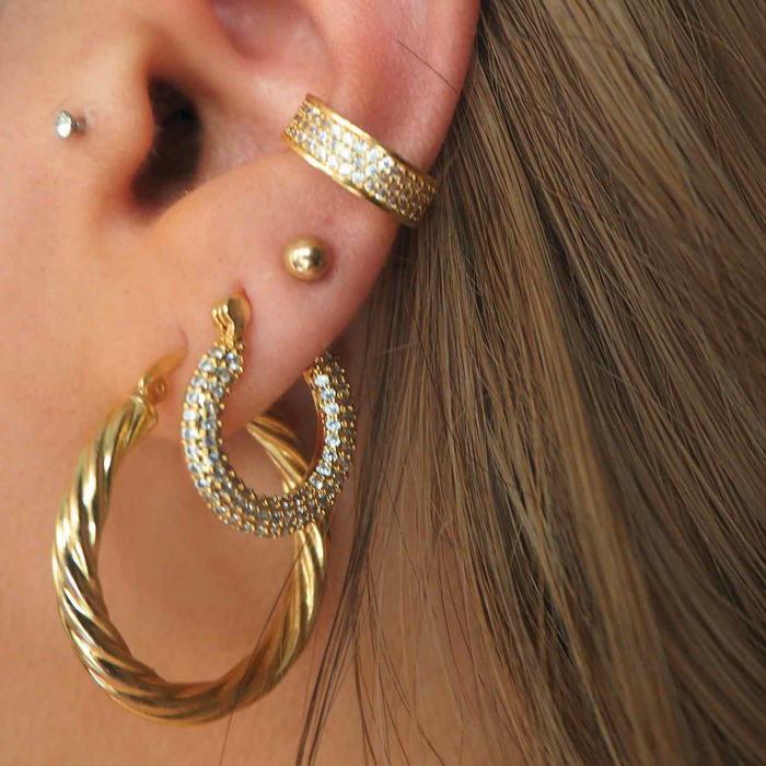 Close-up of an ear with multiple gold and crystal earrings