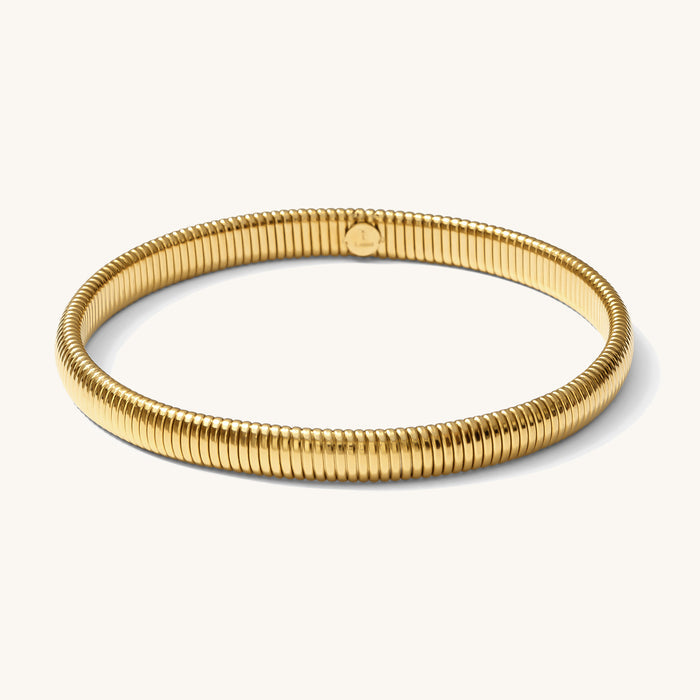 Close up of a gold ribbed bangle bracelet on a white background