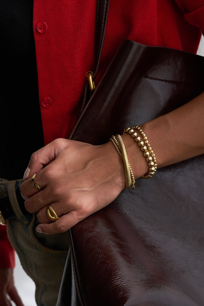 A person in a red cardigan wearing gold jewelry and carrying a brown purse