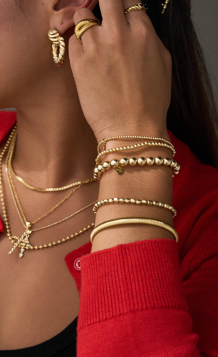 A person wearing a red sweater, black top, and assorted gold jewelry
