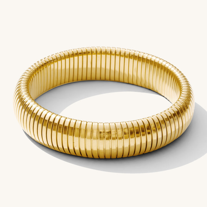 Close up of a gold ribbed bangle bracelet on a white background