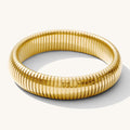 Close up of a gold ribbed bangle bracelet on a white background