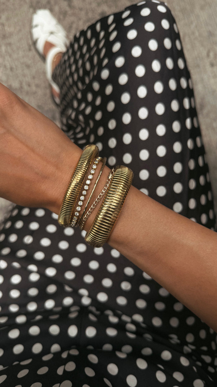 A person wearing a black polka dot skirt and gold bracelets