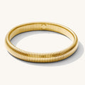 Close up of a gold ribbed bangle bracelet on a white background