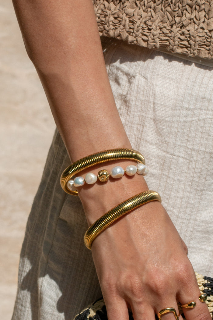 A person in linen pants wearing gold and pearl bracelets and rings