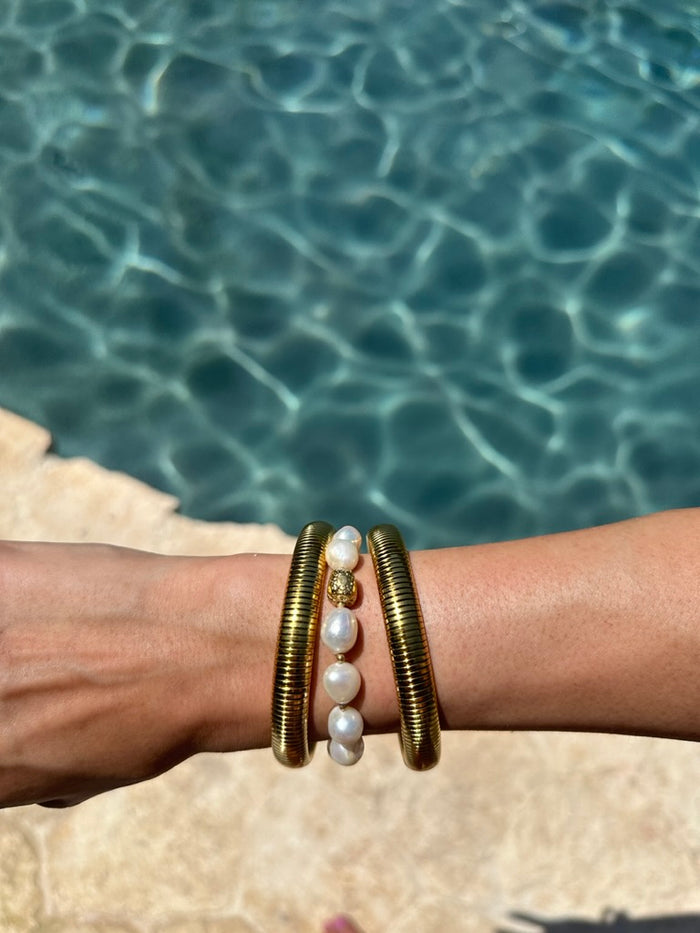 A wrist with gold and pearl bracelets on a pool background