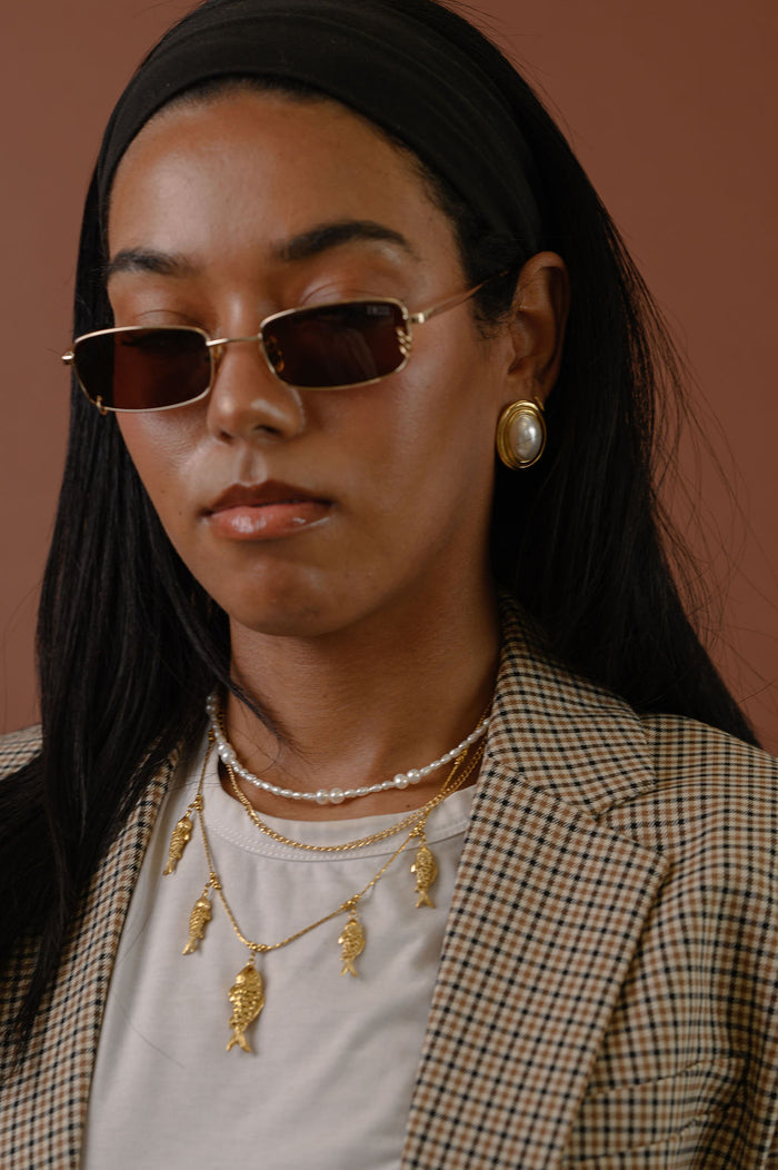 A woman in a blazer wearing statement gold earrings, sunglasses, and necklaces