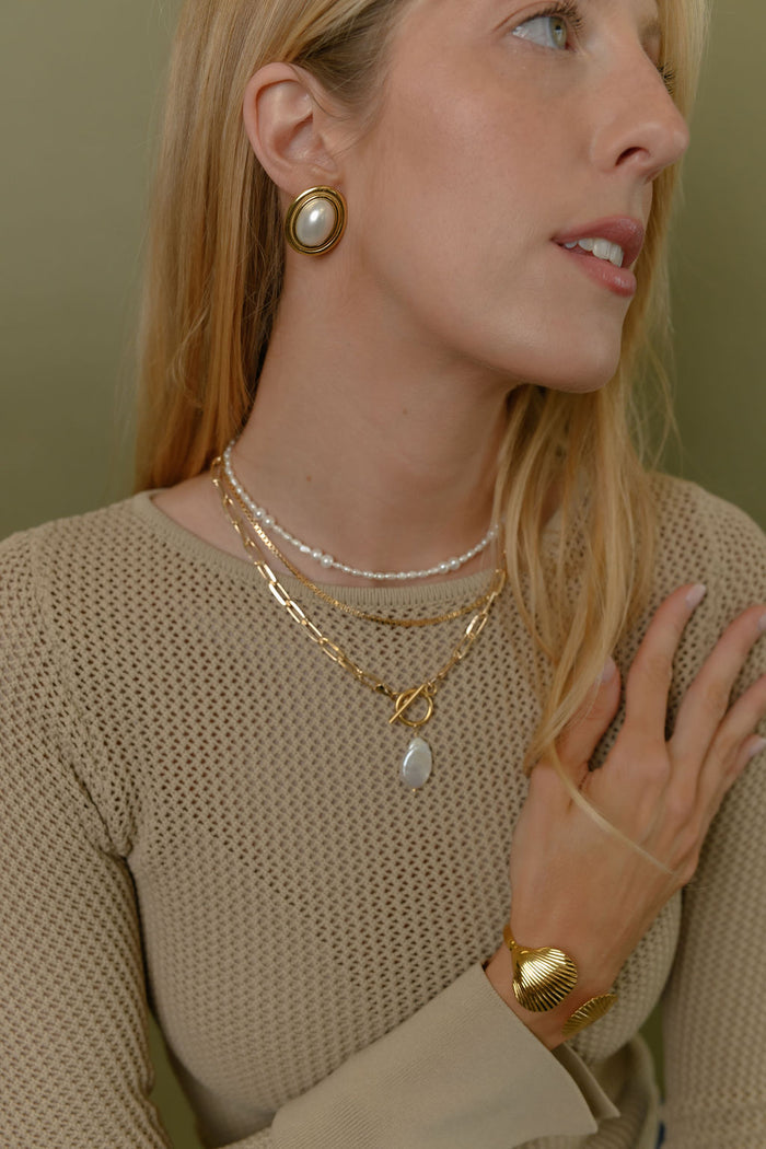 A woman wearing white and gold earrings against a green background